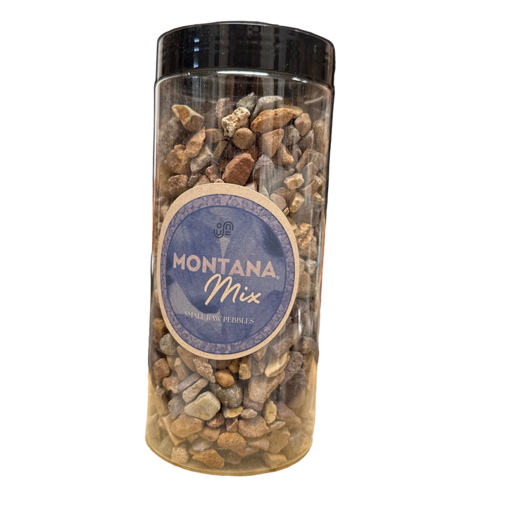 A clear plastic jar filled with Montana Mix gravel and pebble landscaping material, featuring a blue and beige circular label and a black lid, set against a plain white background.